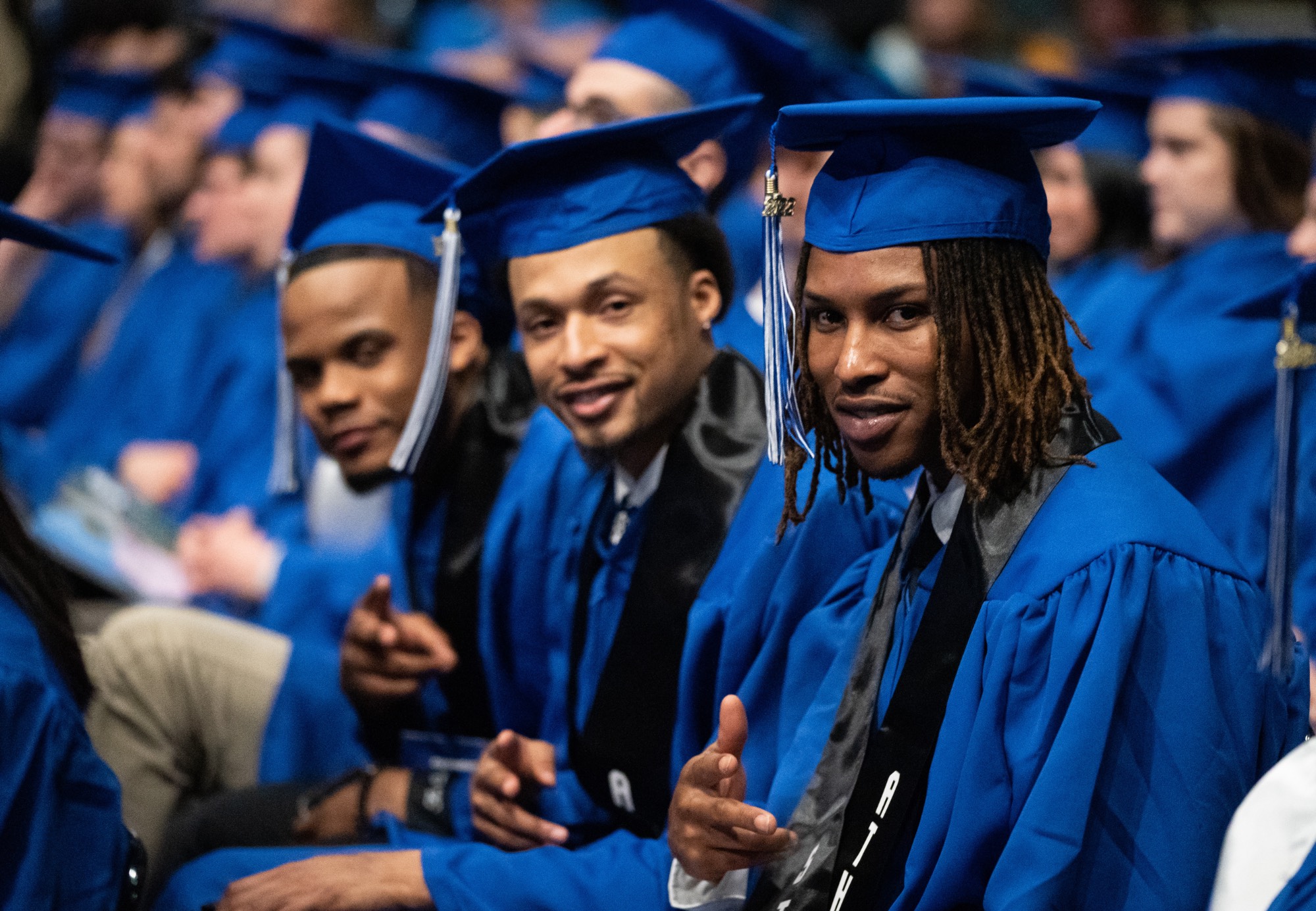 students smiling and pointing at camera at commencement